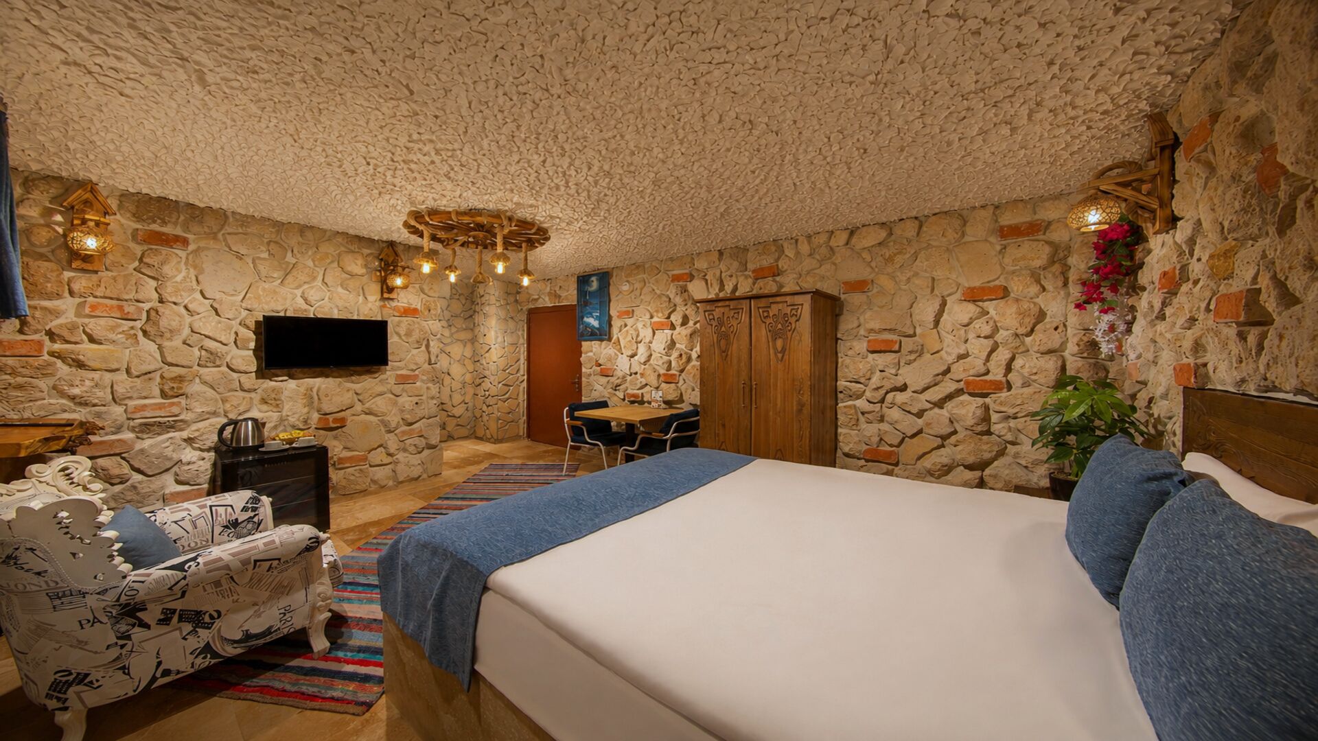 A bedroom with a stone wall, a bed, a desk, a chair, and a television.