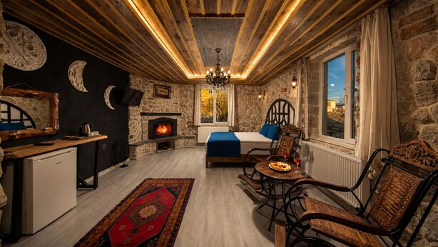 A cozy room with a stone fireplace, a bed with a blue blanket, and a dining area with a table set for two. - Moonlight  Of Cappadocia (Nevsehir)