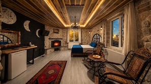 A cozy room with a stone fireplace, a bed with a blue blanket, and a dining area with a table set for two. - Moonlight Of Cappadocia (Nevsehir)