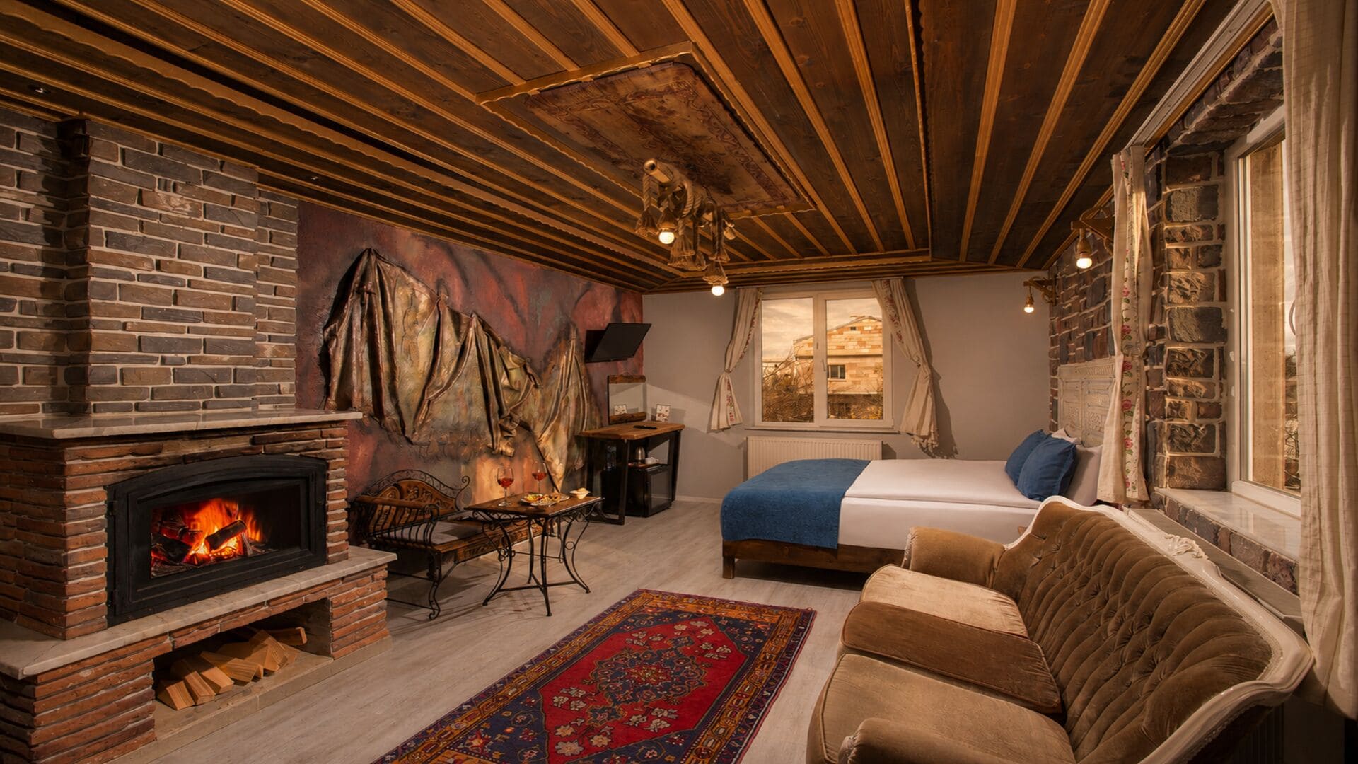 Una habitación acogedora con chimenea, cama, sofá y ventana con cortinas.