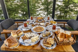 Une table dressée avec différents plats et boissons, probablement pour un repas, avec vue sur les arbres à travers de grandes fenêtres.