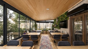 Una habitación amplia con ventanas grandes, techo de madera y una mesa central rodeada de sillas.