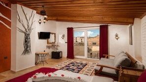A bedroom with a bed, a TV, a desk, a chair, a balcony with a view, and a patterned rug. - Moonlight  Of Cappadocia (Nevsehir)