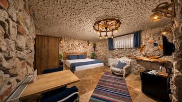 A rustic room with a stone wall, a bed with blue bedding, a wooden table, a patterned rug, and a unique ceiling light fixture.