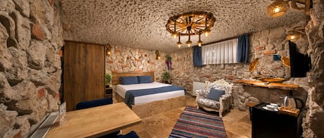 Una habitación rústica con pared de piedra, cama con ropa de cama azul, mesa de madera, alfombra estampada y una lámpara de techo original.