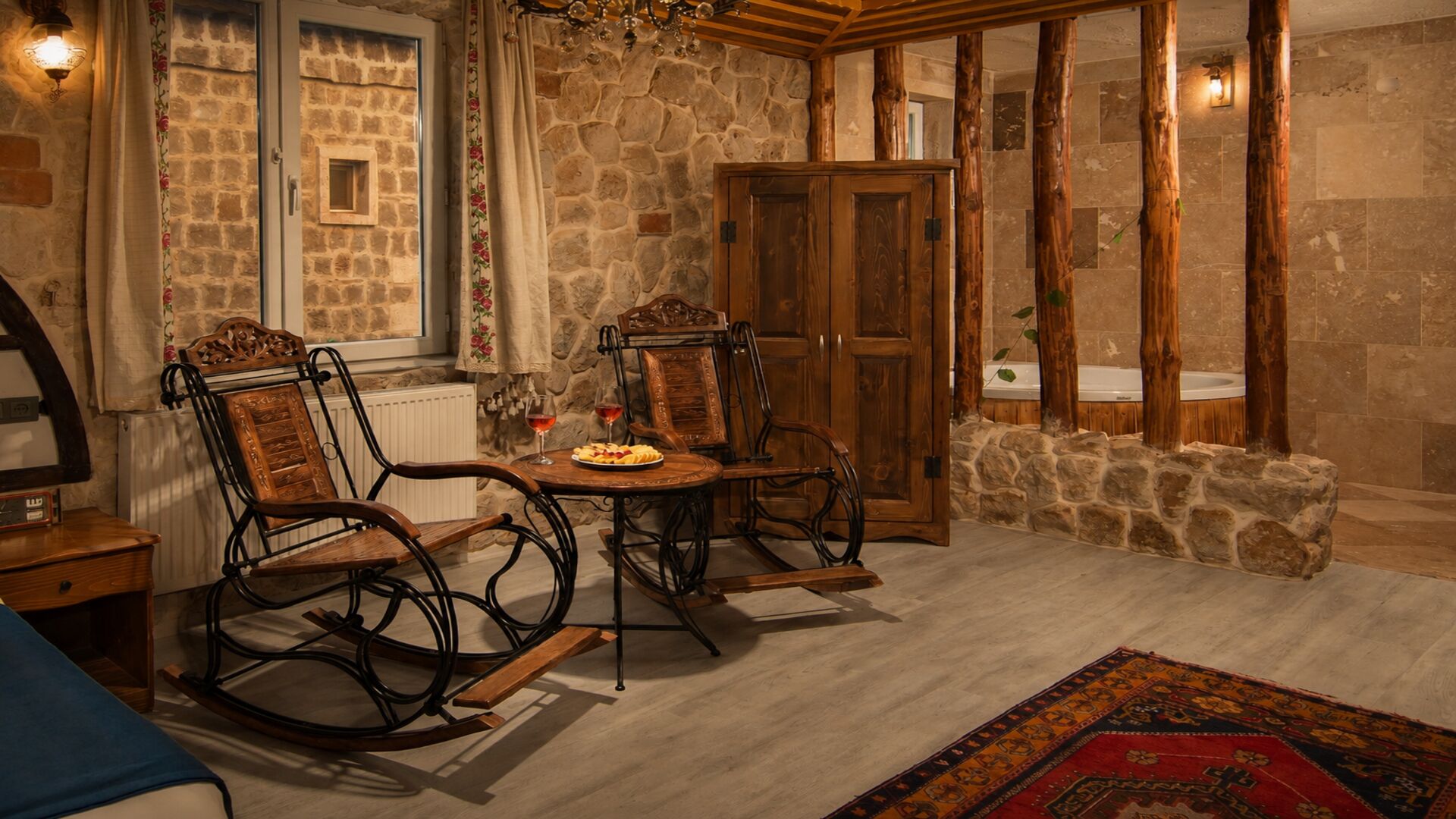 Ένα άνετο δωμάτιο με έναν πέτρινο τοίχο, έπιπλα από ξύλο, ένα τραπέζι φαγητού και ένα πέτρινο παγκάκι.