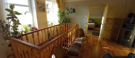 A cozy living room with a wooden staircase, a fireplace, and a view into the adjacent bedroom.
