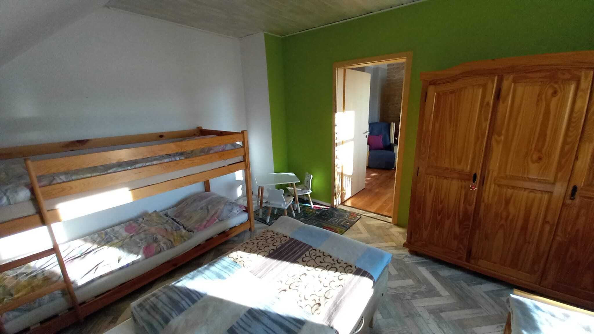 Une pièce comprenant un lit superposé, une petite table avec des chaises, une armoire et une porte donnant sur une autre pièce.