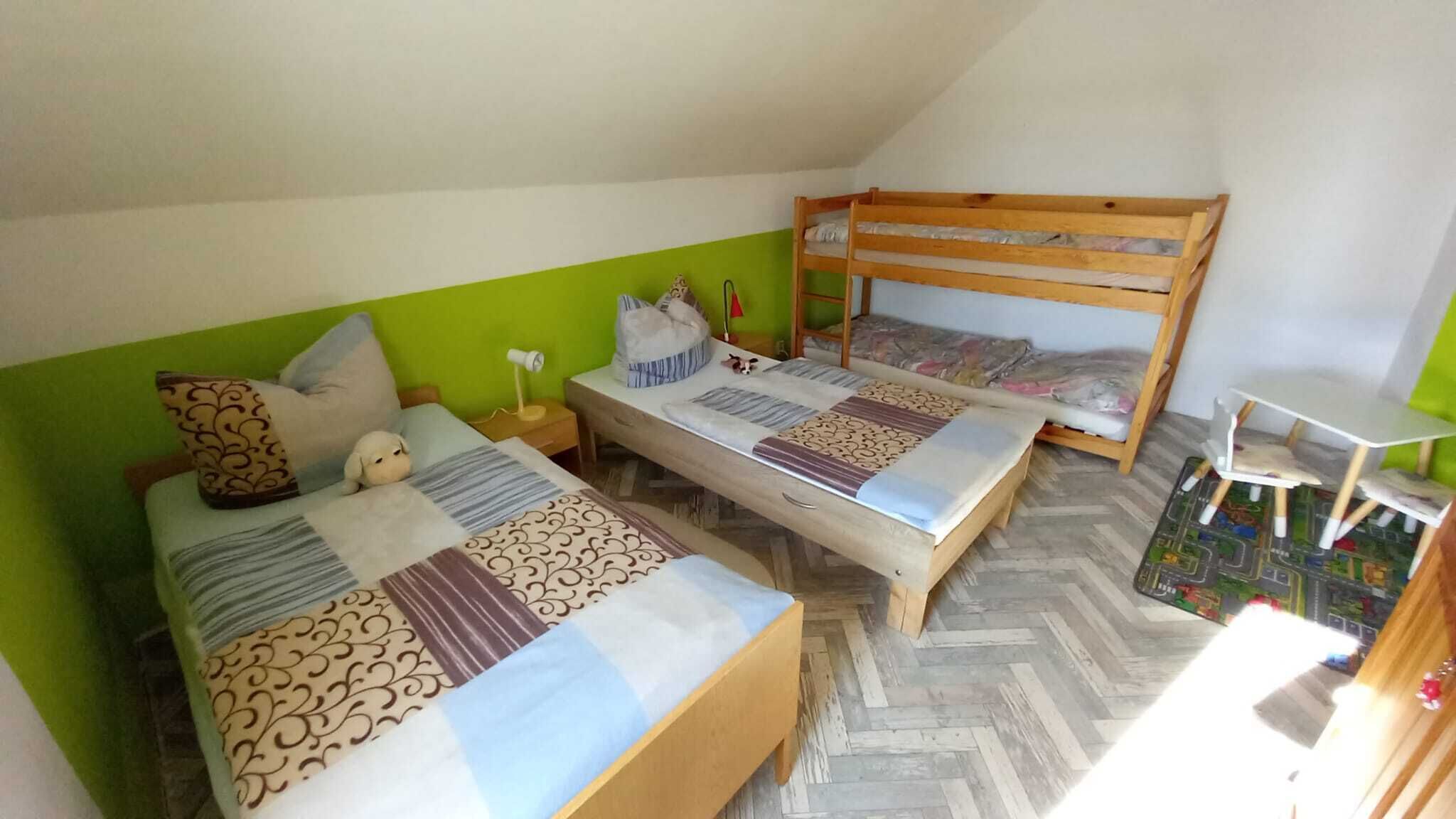 A dormitory room with two beds, a bunk bed, a small table, and a chair.