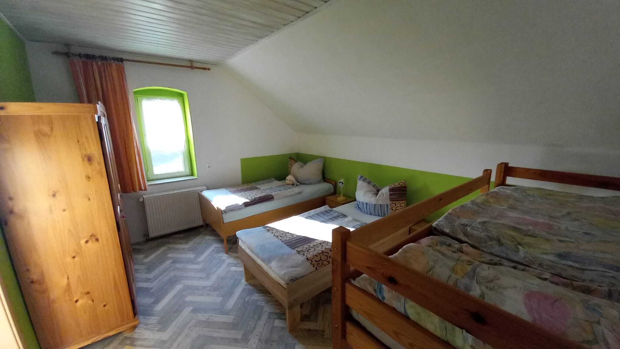 Enkel indkvartering med et enkelt rum, to træsenge, en radiator, et vindue med gardiner og et træskab.