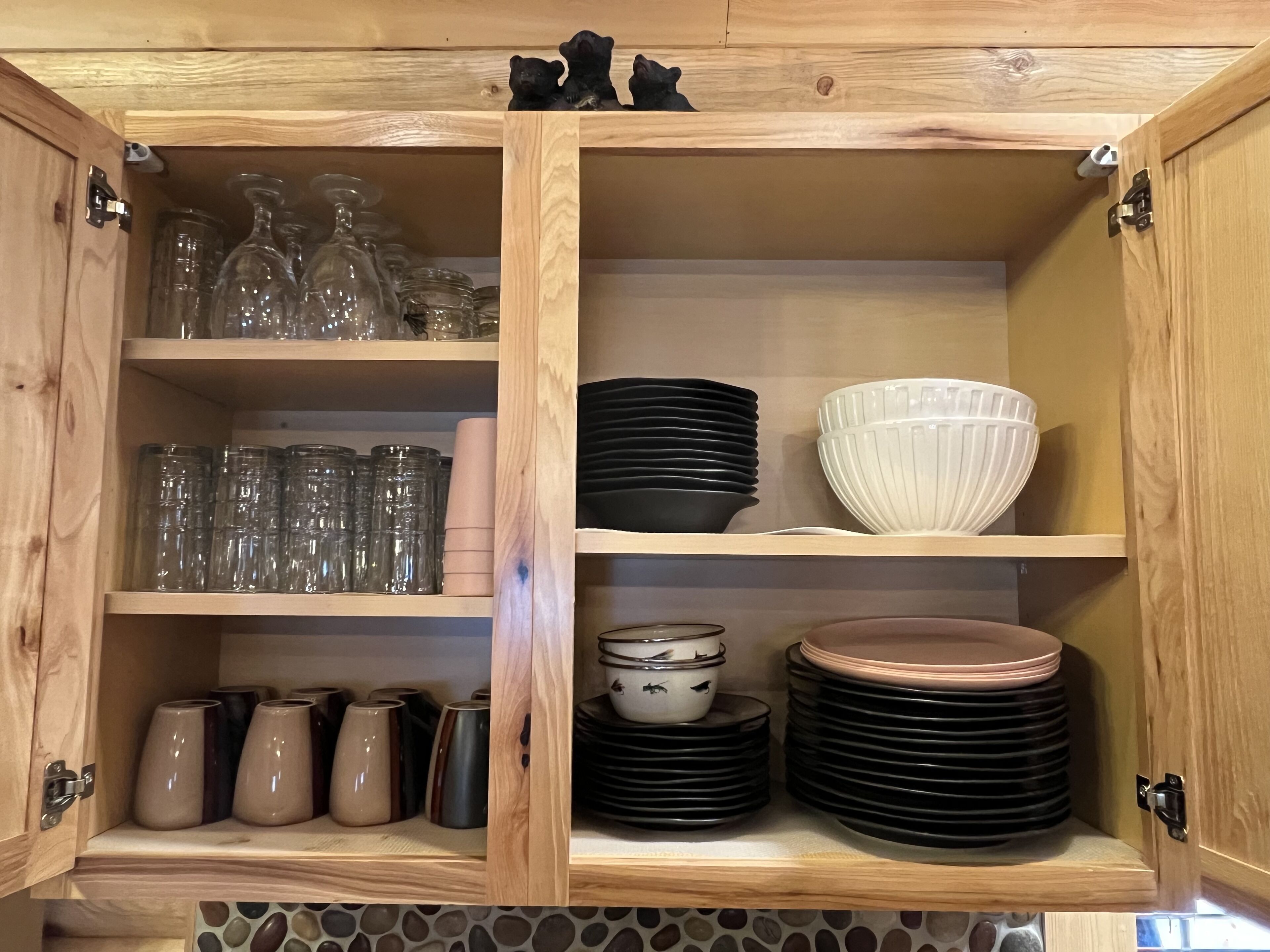 A wooden cabinet with shelves containing glassware, plates, and bowls.