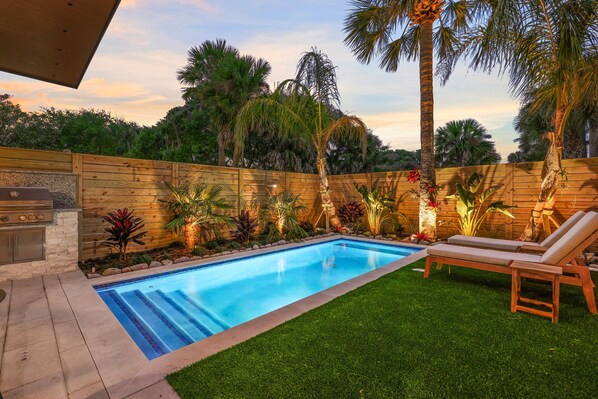 A backyard with a swimming pool, wooden deck, and lounge chairs.
