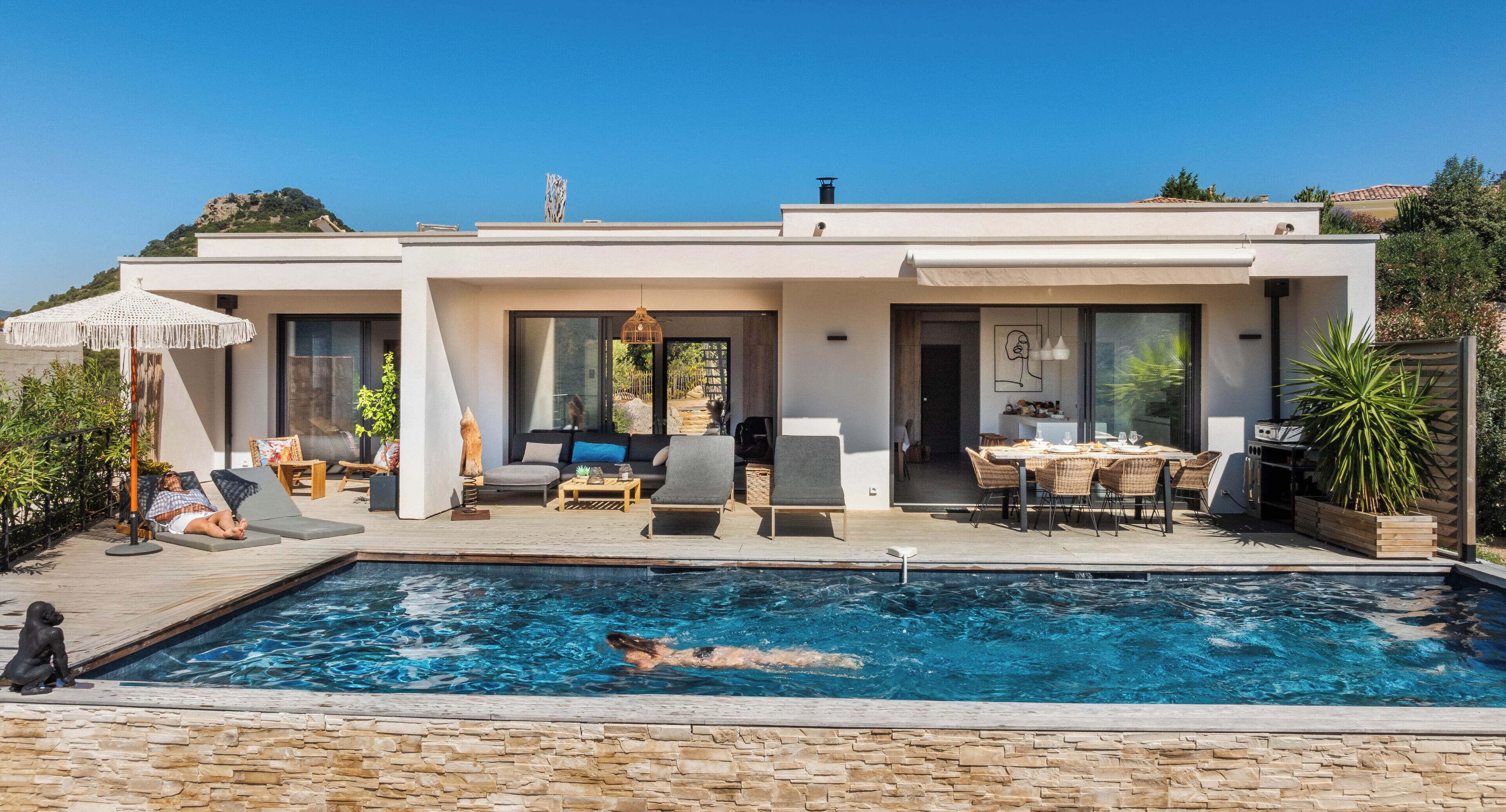 A modern house with a swimming pool, outdoor furniture, and a dining area.