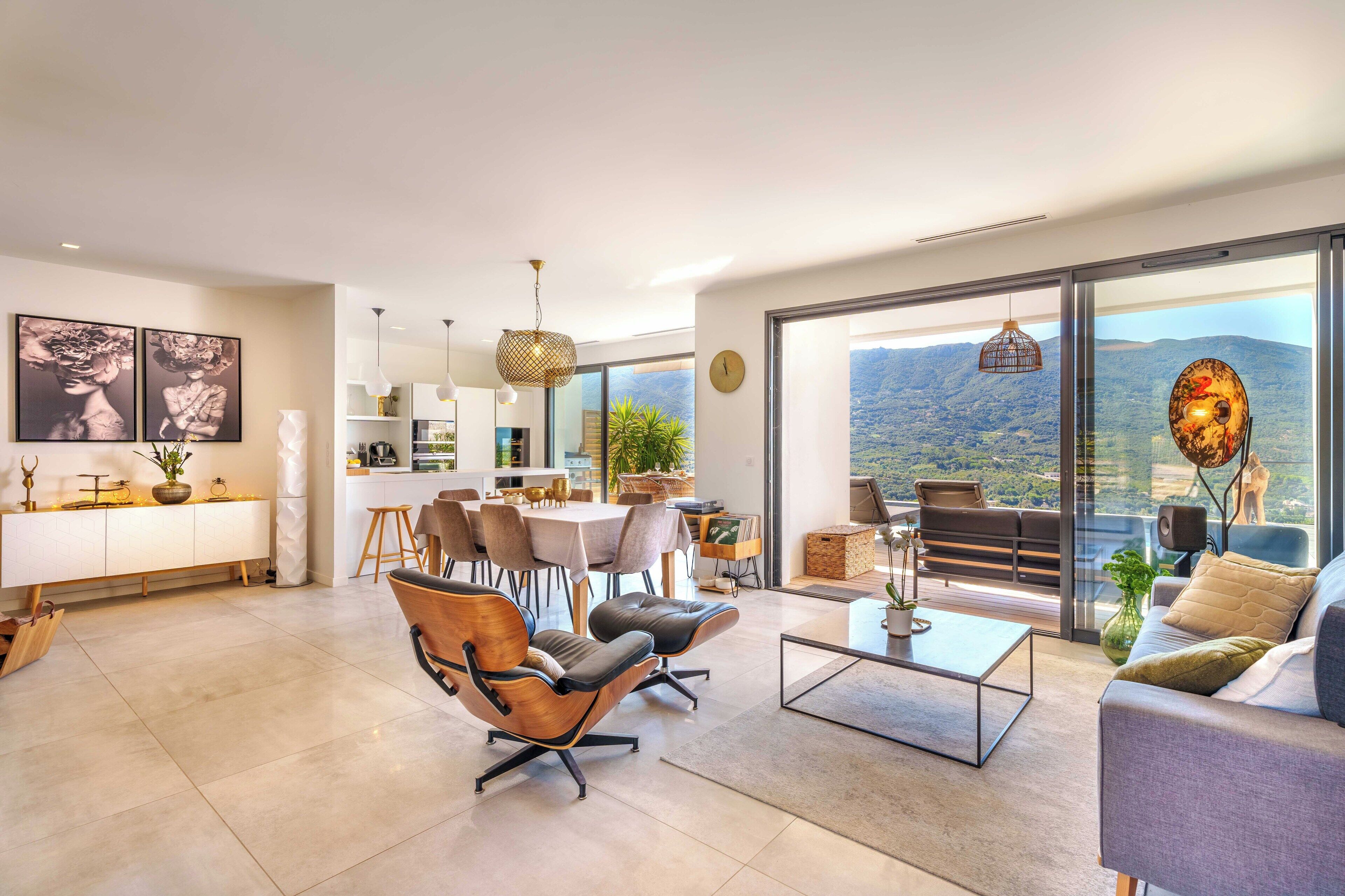 Un vaste espace de vie aménagé avec des meubles modernes, un coin repas et un balcon offrant une vue sur les montagnes.