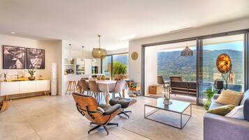 Un vaste espace de vie aménagé avec des meubles modernes, un coin repas et un balcon offrant une vue sur les montagnes.