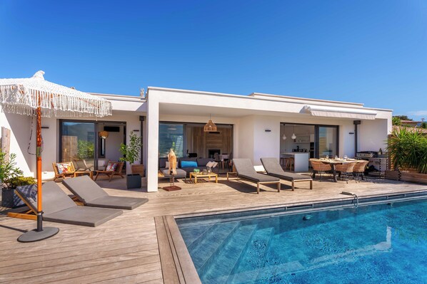 A modern house with a pool, lounge chairs, and a dining area.