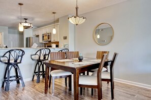 Modern kitchen with central island, microwave, and sink, complemented by pendant lighting and a dining area with wooden table and chairs.