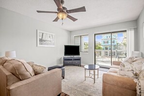 Relax in this inviting living room with a flat-screen TV, ceiling fan, and stunning views of the surrounding greenery.