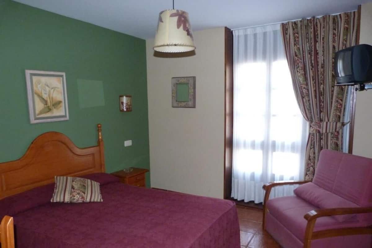 A room with a bed, a chair, a television, and a window with curtains.