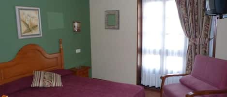 Ein Zimmer mit einem Bett, einem Sessel, einem Fernseher und einem Fenster mit Vorhängen.