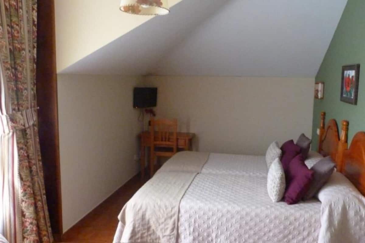 A bedroom with a bed, a chair, a television, and a window with curtains.