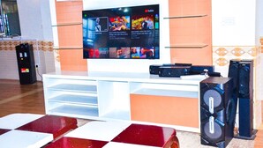 Una sala de estar moderna con un televisor de pantalla plana montado sobre un mueble blanco, una cafetera y un par de altavoces.