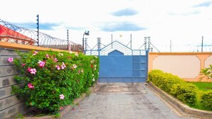 Un sendero pavimentado que conduce a una entrada portonada con un portón azul, rodeado de follaje y un muro de piedra.