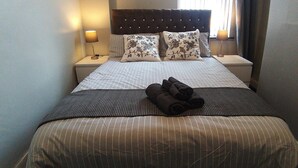 Ein ordentlich bezogenes Bett mit gestreifter Bettwäsche, zwei blumigen Kissen und einem gefalteten Handtuch.