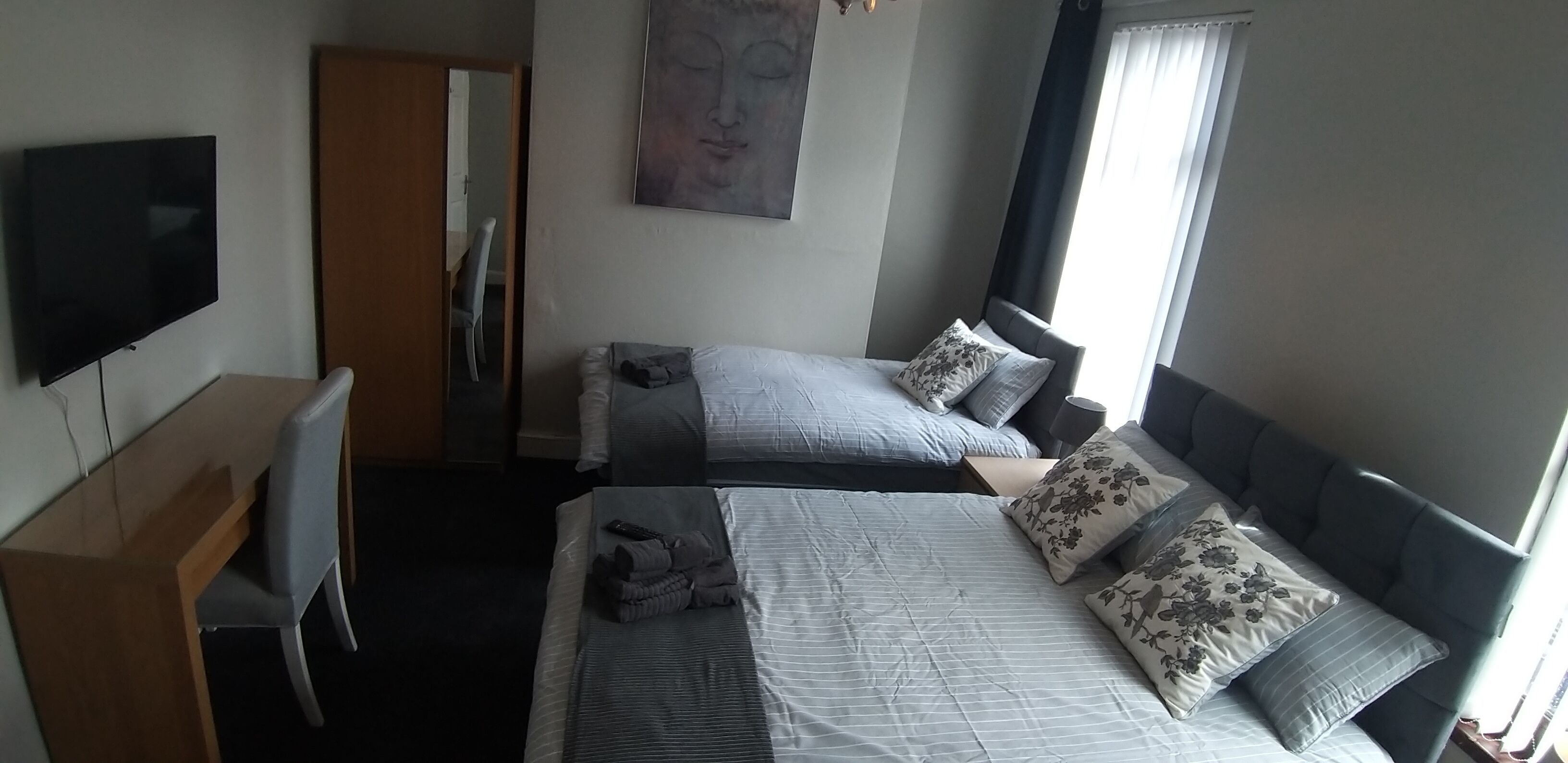 Une chambre d’hôtel avec deux lits, un bureau, une chaise, une télévision et une fenêtre avec des rideaux.