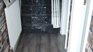 Ein Korridor mit grauem Holzboden, weißen Fußleisten und einer Ziegelwand an einer Seite.