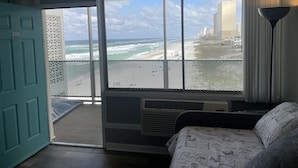 A room with a large window overlooking a beach and ocean, a balcony with a metal railing, a door with a number, and a patterned bedspread. - Studio condo on beach at Historical Fontainebleau Terrace. Sleeps 4.Full Kitchen (Panama City Beach)