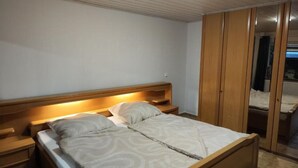 Een slaapkamer met een houten bed, nachtkastjes, een kledingkast en een plafondlamp.