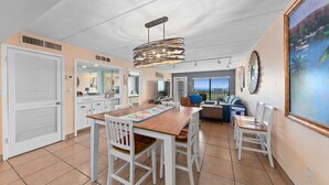 A spacious dining area with a wooden table and white chairs, a modern pendant light, and a view of the ocean through large windows.