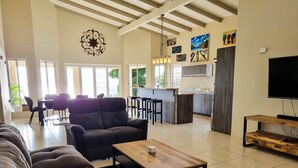 A spacious living room with a large sofa, a coffee table, and a TV. There is a dining area with chairs and a table, and a kitchen in the background. - Villa with Private Pool and Jacuzzi / Sea View (Cas Abou)