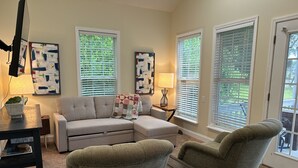 A living room with a sectional sofa, two armchairs, a coffee table, and a small side table with a lamp. There are three windows with blinds, and artwork is displayed on the walls. - The Lake is Callling you to Creek Cabin (Warwick)
