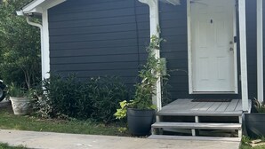 A dark-colored single-story house with a white door and a small porch. - The Lake is Callling you to Creek Cabin (Warwick)