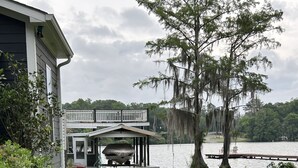 A house with a covered deck overlooking a lake, surrounded by lush greenery and a stone pathway. - The Lake is Callling you to Creek Cabin (Warwick)