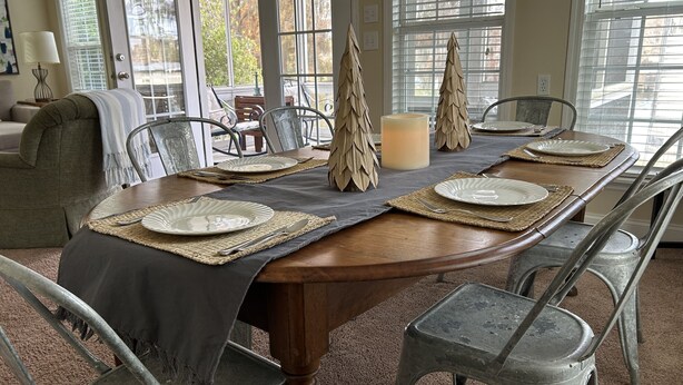 A dining table set with plates, cutlery, and a candle, surrounded by metal chairs in a room with large windows and a carpeted floor. - The Lake is Callling you to Creek Cabin (Warwick)