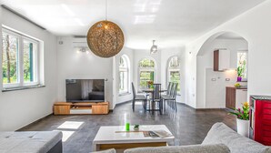 A modern living room with a flat-screen TV, a dining area with chairs, and a kitchen area with cabinets. - Awesome home in Labin (Labin)