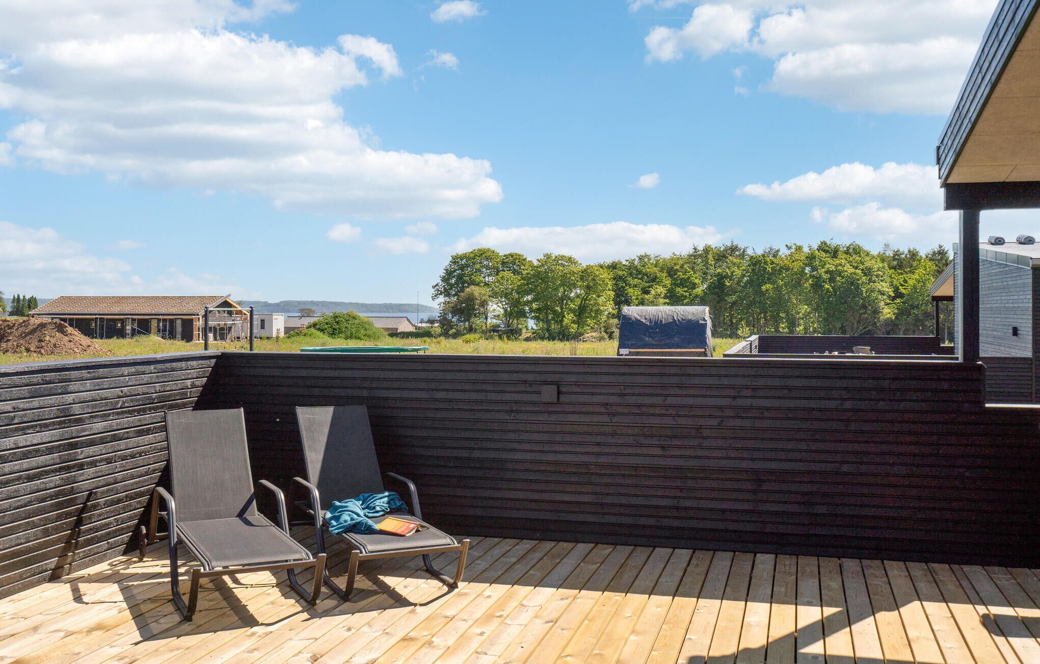 A wooden deck with two lounge chairs and a table, overlooking a landscape with trees and buildings.