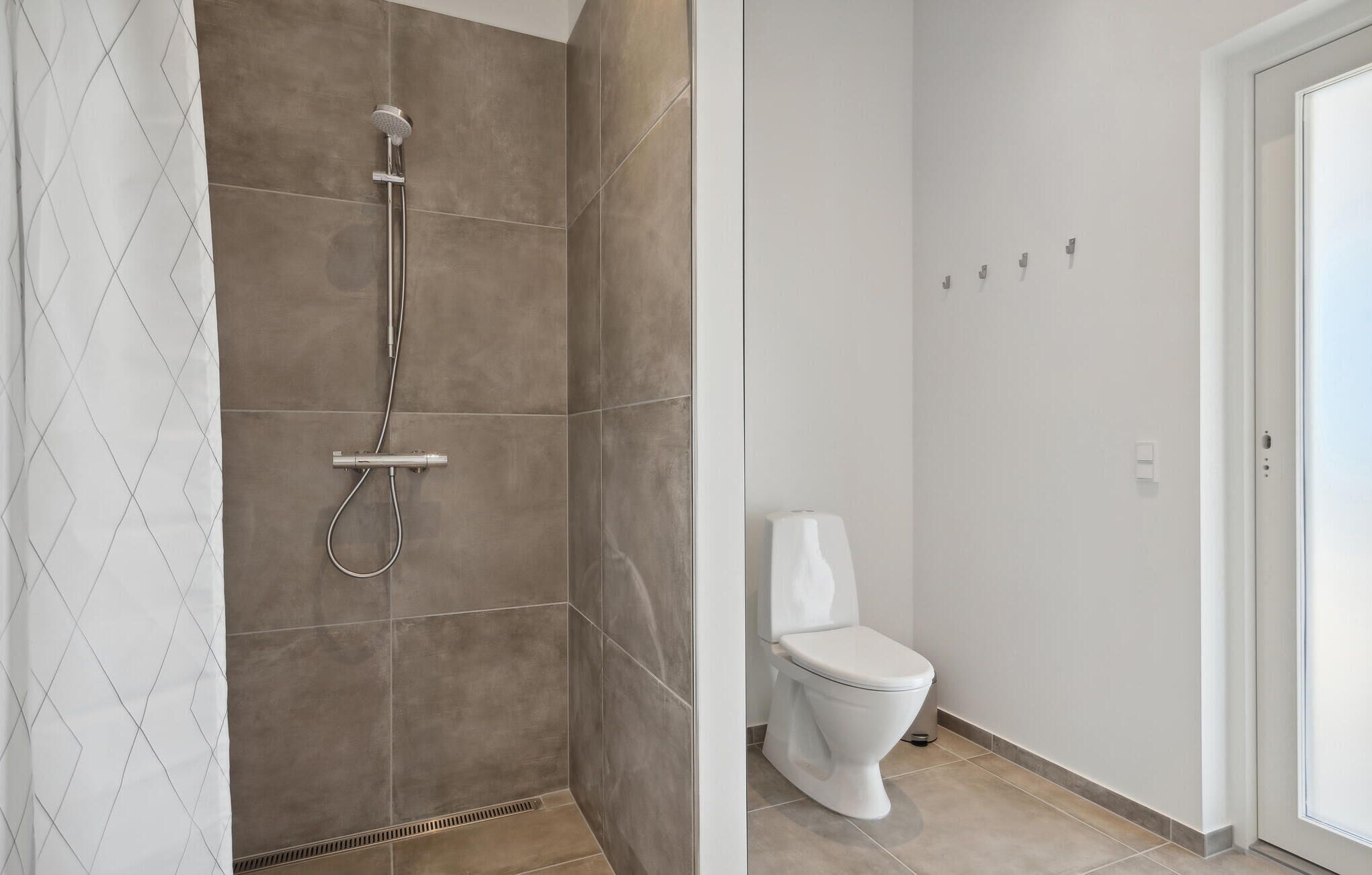 Een badkamer met een douche, toilet en een witte deur.
