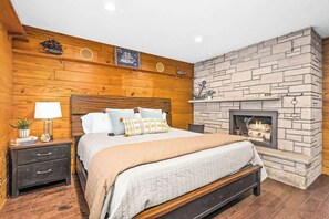 Une chambre avec une cheminée en pierre, des murs en bois, un lit avec des oreillers, une table de chevet avec une lampe et une petite étagère avec des objets décoratifs.
