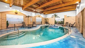 Una piscina interior con vigas de madera, sillones de descanso y vistas al mar a través de un amplio ventanal.