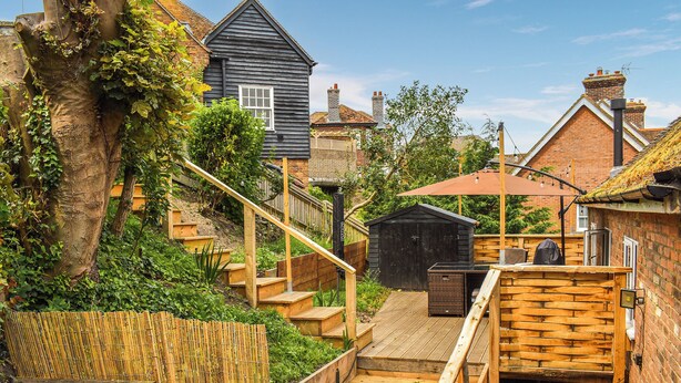 A wooden staircase leading to a backyard with a garden, a small shed, and a house with a sloped roof. - 2 bedroom accommodation in Rye (Rye)