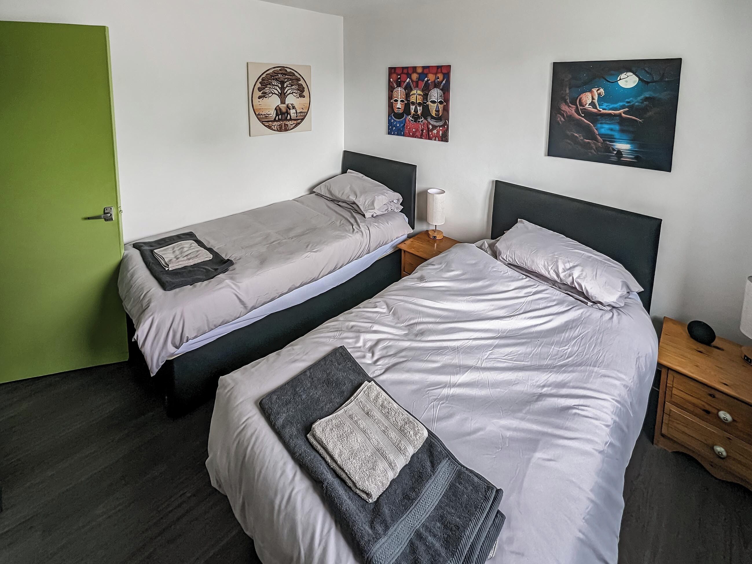 A room with two beds, a green door, and three artworks on the wall.