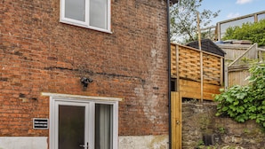 A brick building with a white door, a window, and a wooden structure in the background. - 2 bedroom accommodation in Rye (Rye)
