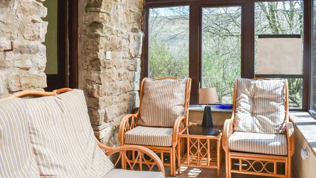 A room with a stone wall, wicker furniture, and large windows offering a view of trees. - 2 bedroom accommodation in Snaizeholme, near Hawes (Snaizeholme, near Hawes)