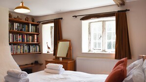 A bedroom with a large bed, a bookshelf, a mirror, and two windows with curtains. - 3 bedroom accommodation in Skelton, near Penrith (Skelton, near Penrith)