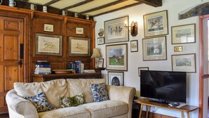 A cozy living room with a sofa, coffee table, and a television. There are framed pictures on the wall and a wooden cabinet with books. - 3 bedroom accommodation in Skelton, near Penrith (Skelton, near Penrith)
