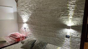 A room with a stone wall, a bed with patterned bedding, and two wall-mounted lights. - LA GHIANDA APPARTAMENTO CON TERRAZZO ANIMALI AMMESSI (Cossogno)